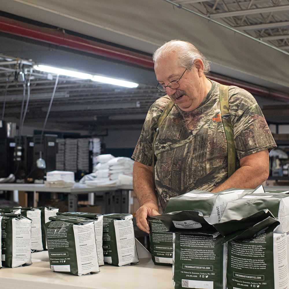 A man smiling, packing green coffee.